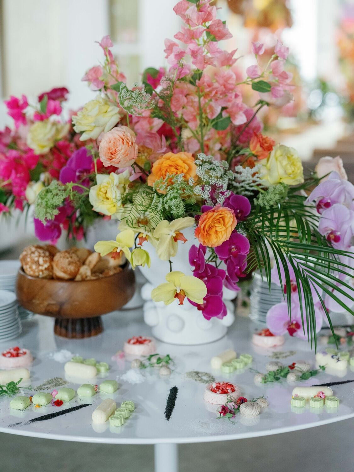 WPC Wedding Catering Vibrant tropical floral centerpiece with orchids, roses, and bougainvillea surrounded by elegant petit fours at a luxury anniversary event