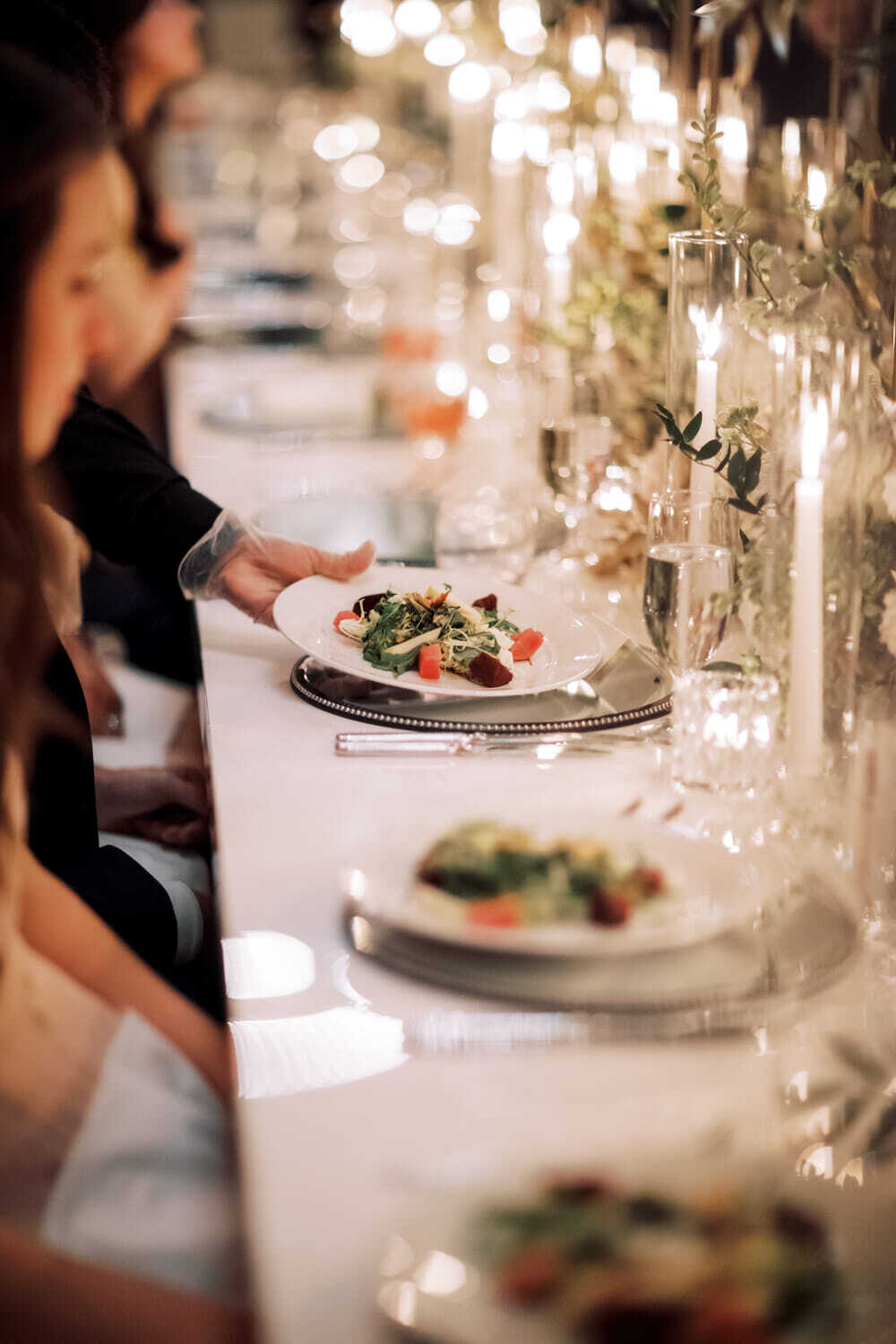 WPC Wedding Catering Server presenting a plated salad course at an elegantly set wedding reception dinner table with candlelight and crystal glassware