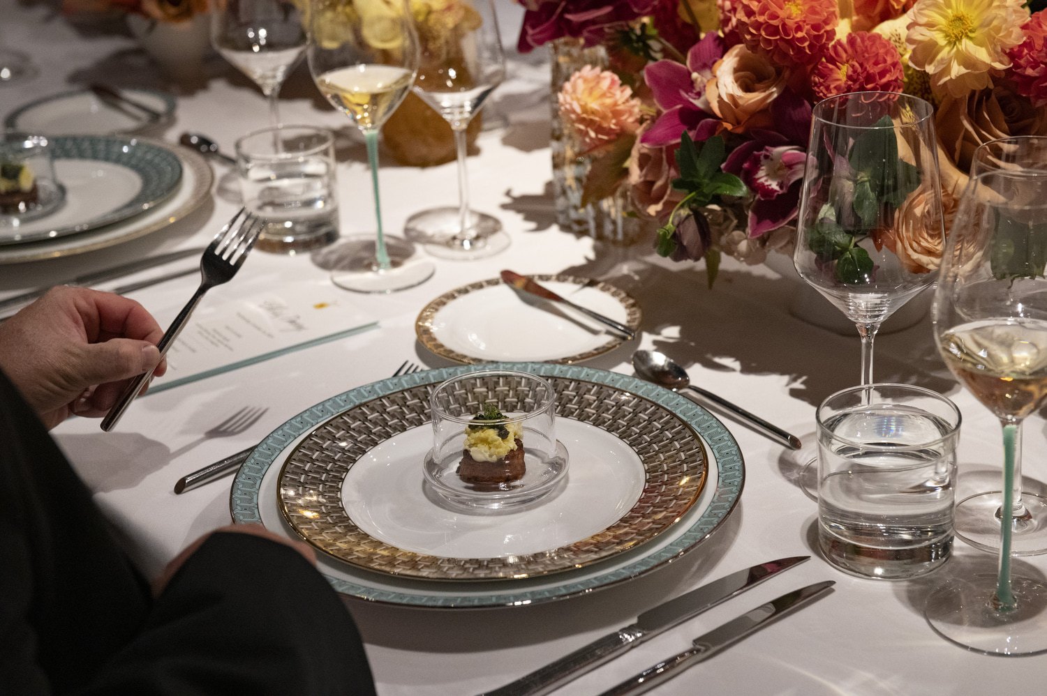 WPC Wedding Catering Elegant formal dinner place setting with ornate china, amuse-bouche under glass, crystal wine glasses, and a floral centerpiece at a luxury gala