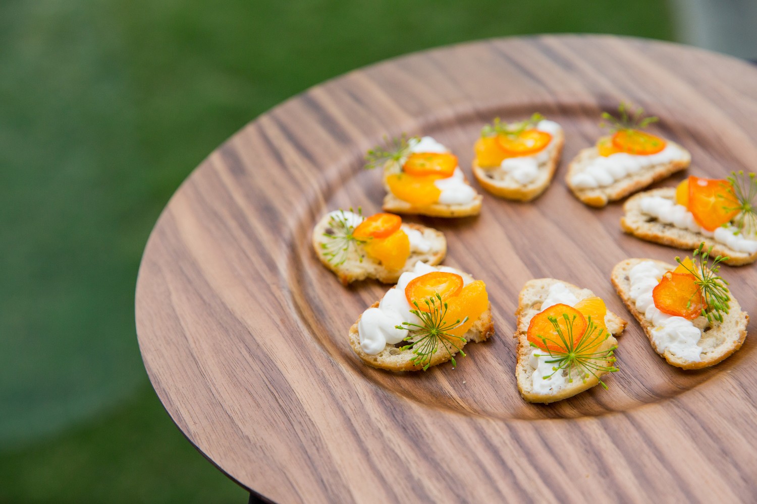 WPC Wedding Catering Gourmet crostini appetizers with whipped ricotta, kumquat, and fresh dill arranged on a walnut wood board at an outdoor catered event