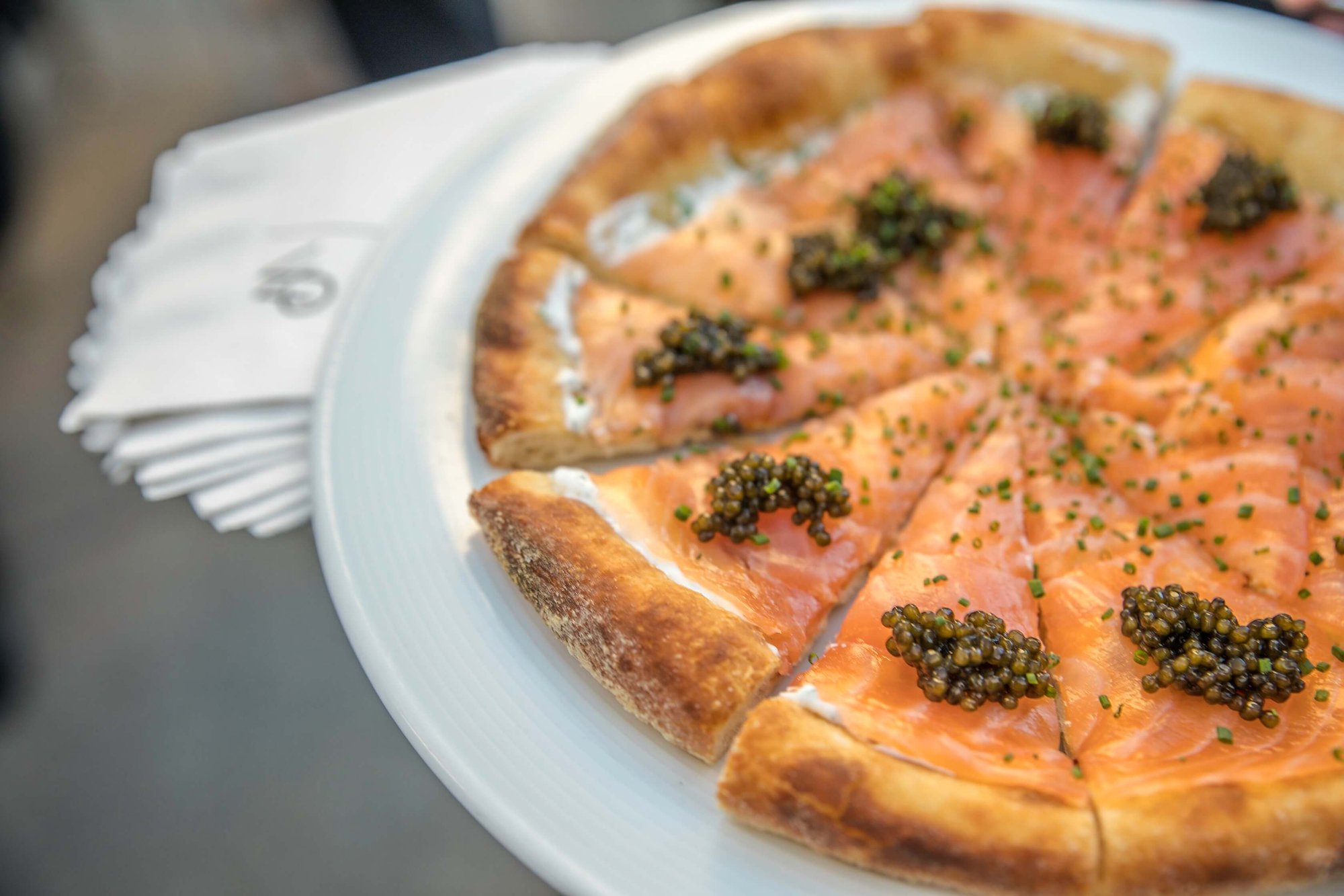 Wolfgang Puck's iconic smoked salmon pizza topped with black caviar and fresh chives, sliced and plated on a white dish